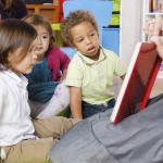 Tre barn ser i bok som barnehagelærer holder opp foran dem